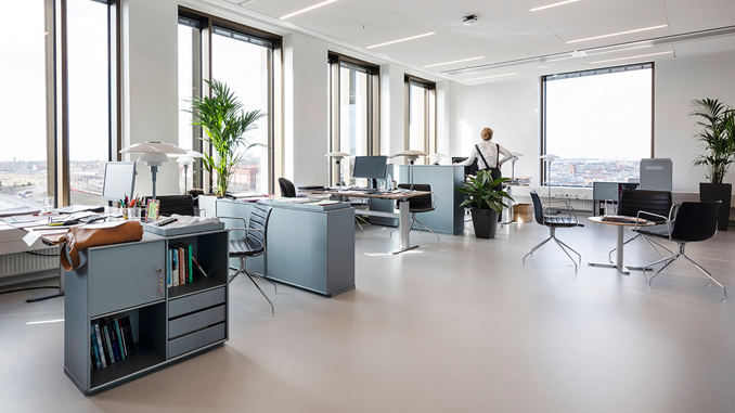 Et åbent kontor med skriveborde adskilt af reoler og potteplanter i det fællesstatslige kontorknudepunkt Kalvebod Brygge i København.