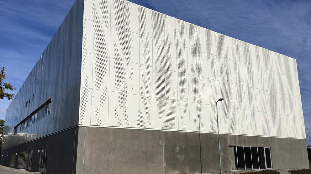 DTU Large Scale Facility med grå sokkel i stueniveau og lys facade med kunstnerisk mønster på de øvrige etager. Bygningen har meget få vinduer.