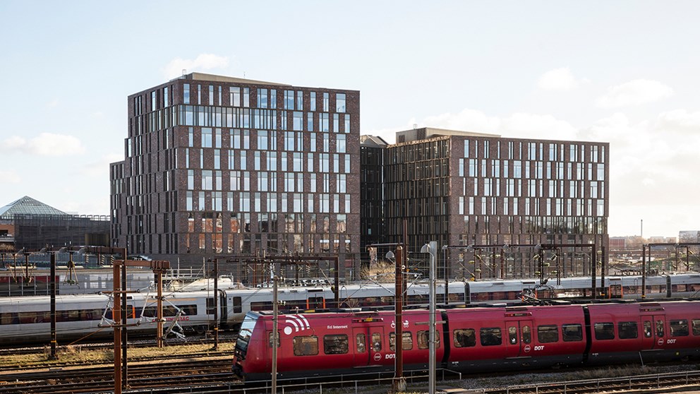 To af fire tårne af kontorknudepunktet NEXUS på Kalvebod Brygge set fra modsatte side af baneterrænnet. Der kører to toge på banen foran