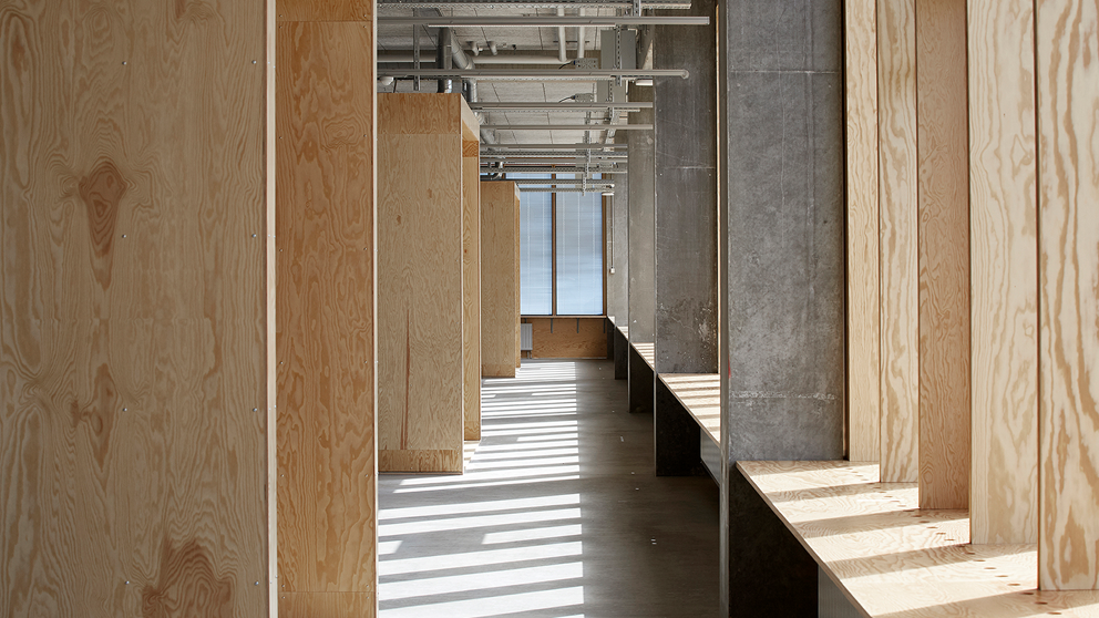 Beton, træ og synlige installationer i loftet indvendigt på den nye arkitektskole i Aarhus