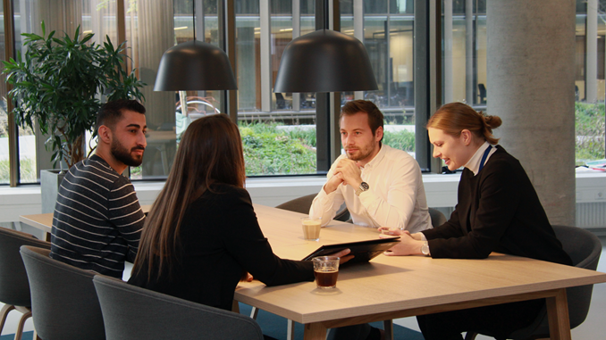 Fleksible mødefaciliteter hos Bygningsstyrelsen. Her sidder fire medarbejdere og holder møde om et langbord og taler om det, de ser på den bærbare PC.