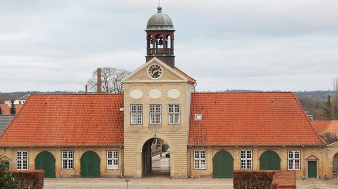 Sidebygning til Augustenborg Slot i gule mursten, rødt tegltag og grønne afrundede døråbninger samt tårn på toppen