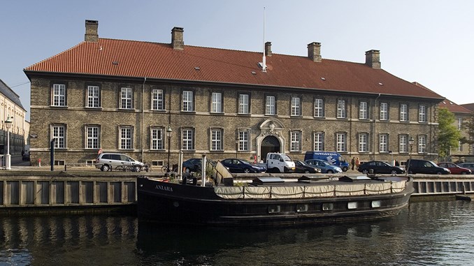 Frederiksholms Kanal 21-23 i København set fra den modsatte side af kanalen. Der ligger et skib til kaj foran hovedindgangen i den gule murstensbygning med rødt tegltag.