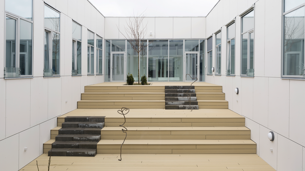 Maria Zahles kunstværk i bronze til Institut for Energiteknik, Aalborg Universitet. Kunstværket lægger sig op ad trinene på en udendørs trappe i træ.