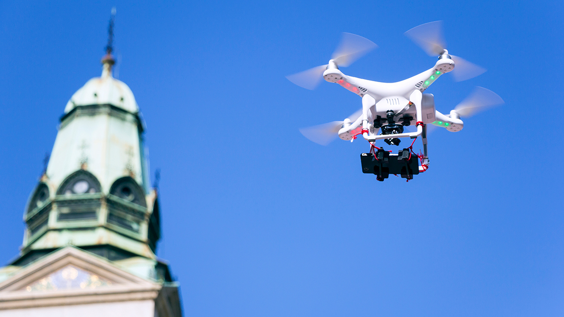 Drone svæver med kobbergrønt tårn og blå himmel i baggrunden